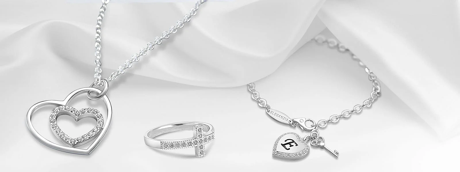 Front Page -Jewelry Sales Store Silver heart necklace cross ring and charm bracelet on white fabric